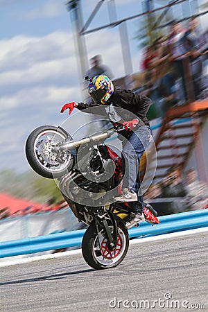 The stuntman shows tricks on a motorcycle while standing on it on one wheel with one foot and driving with one hand Editorial Stock Photo