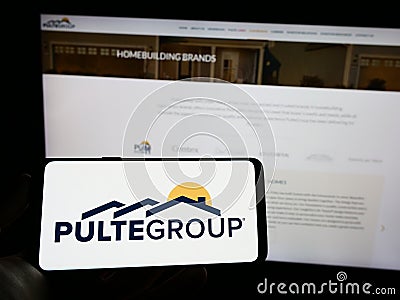 Person holding cellphone with logo of American home construction company PulteGroup Inc. on screen in front of webpage. Editorial Stock Photo