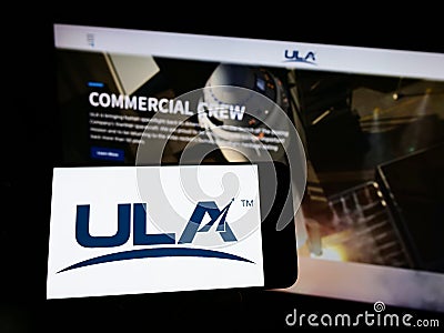 Person holding cellphone with logo of American space company United Launch Alliance (ULA) on screen in front of webpage. Editorial Stock Photo