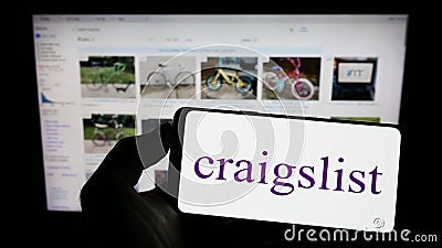 Person holding cellphone with logo of classified advertisements company Craigslist Inc. on screen in front of webpage. Editorial Stock Photo