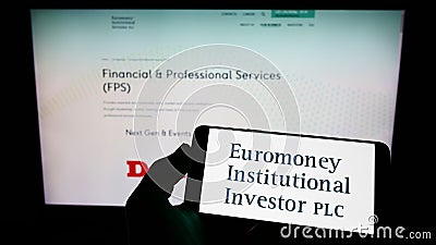 Person holding cellphone with logo of company Euromoney Institutional Investor plc on screen in front of business webpage. Editorial Stock Photo