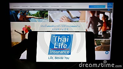 Person holding cellphone with logo of company Thai Life Insurance Public Co. Ltd. on screen in front of business webpage. Editorial Stock Photo