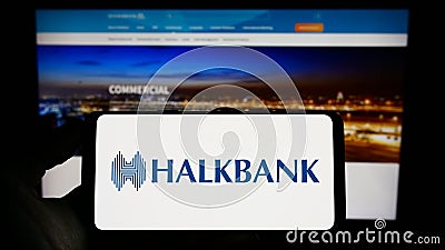 Person holding cellphone with logo of company Turkiye Halk Bankasi A.S. (Halkbank) on screen in front of webpage. Editorial Stock Photo