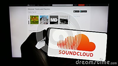 Person holding cellphone with logo of German music sharing company SoundCloud on screen in front of business webpage. Editorial Stock Photo