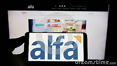 Person holding cellphone with logo of Mexican company Alfa SAB de CV on screen in front of business website. Editorial Stock Photo