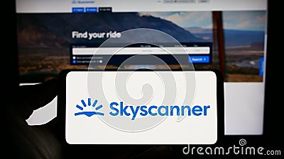 Person holding cellphone with logo of travel metasearch company Skyscanner Ltd. on screen in front of business webpage. Editorial Stock Photo