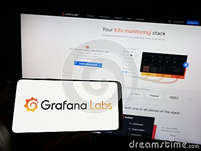 Person holding cellphone with logo of US analytics software company Grafana Labs on screen in front of business webpage. Editorial Stock Photo