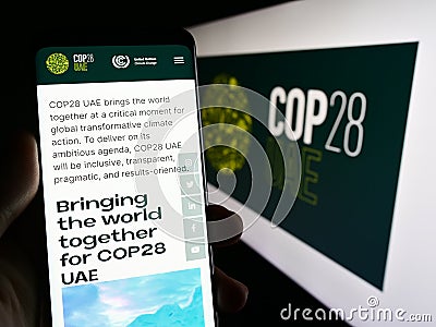 Person holding cellphone with web page of UN climate change conference COP28 (Dubai) on screen in front of logo. Editorial Stock Photo