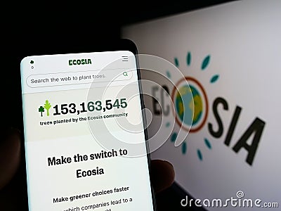 Person holding cellphone with webpage of German search engine company Ecosia GmbH on screen in front of logo. Editorial Stock Photo