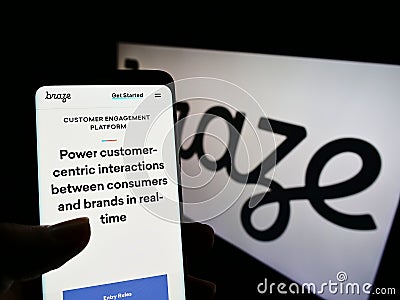 Person holding cellphone with webpage of US marketing software company Braze Inc. on screen in front of logo. Editorial Stock Photo