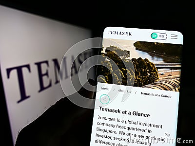 Person holding cellphone with website of company Temasek Holdings Private Limited on screen in front of logo. Editorial Stock Photo