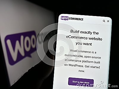 Person holding cellphone with website of open-source e-commerce solution WooCommerce on screen in front of logo. Editorial Stock Photo