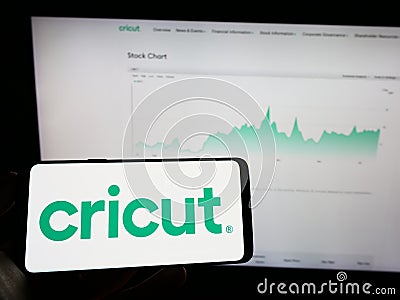 Person holding mobile phone with logo of American cutting plotter company Cricut Inc. on screen in front of web page. Editorial Stock Photo