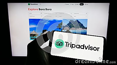 Person holding mobile phone with logo of American travel company Tripadvisor Inc. on screen in front of business web page. Editorial Stock Photo