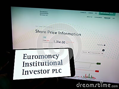 Person holding mobile phone with logo of company Euromoney Institutional Investor plc on screen in front of web page. Editorial Stock Photo