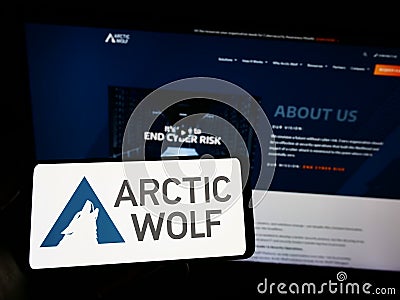 Person holding mobile phone with logo of cybersecurity company Arctic Wolf Networks Inc. on screen in front of web page. Editorial Stock Photo