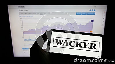 Person holding mobile phone with logo of German chemical company Wacker Chemie AG on screen in front of business web page. Editorial Stock Photo