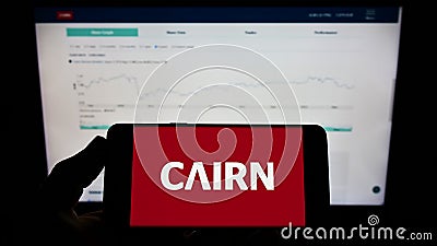 Person holding mobile phone with logo of Irish housebuilding company Cairn Homes plc on screen in front of web page. Editorial Stock Photo