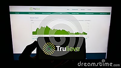 Person holding mobile phone with logo of medical marijuana company Trulieve Cannabis Corp. on screen in front of web page. Editorial Stock Photo