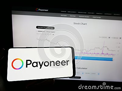 Person holding mobile phone with logo of payments company Payoneer Global Inc. on screen in front of business web page. Editorial Stock Photo