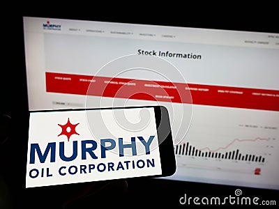Person holding mobile phone with logo of US exploration company Murphy Oil Corporation on screen in front of web page. Editorial Stock Photo