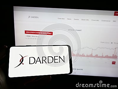 Person holding mobile phone with logo of US gastronomy company Darden Restaurants Inc. on screen in front of web page. Editorial Stock Photo