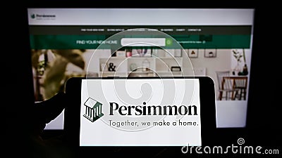 Person holding smartphone with logo of British housebuilding company Persimmon plc on screen in front of website. Editorial Stock Photo