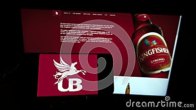 Person holding smartphone with logo of company United Breweries Holdings Limited (UBHL) on screen in front of website. Editorial Stock Photo