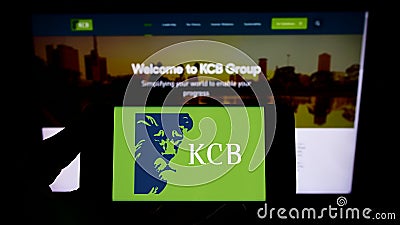 Person holding smartphone with logo of Kenyan financial company KCB Group Limited on screen in front of website. Editorial Stock Photo