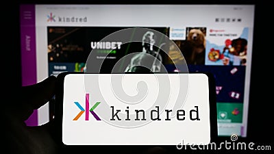 Person holding smartphone with logo of online gambling company Kindred Group plc on screen in front of website. Editorial Stock Photo