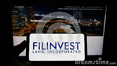 Person holding smartphone with logo of real estate company Filinvest Land Inc. (FLI) on screen in front of website. Editorial Stock Photo