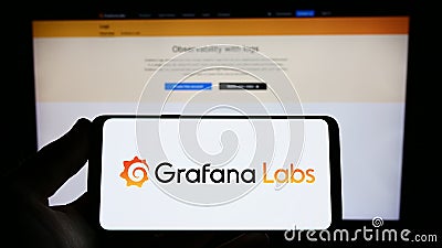 Person holding smartphone with logo of US analytics software company Grafana Labs on screen in front of website. Editorial Stock Photo