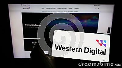Person holding smartphone with logo of US company Western Digital Corporation (WDC) on screen in front of website. Editorial Stock Photo