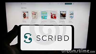 Person holding smartphone with logo of US publishing platform company Scribd Inc. on screen in front of website. Editorial Stock Photo