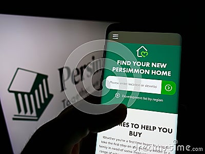 Person holding smartphone with website of British housebuilding company Persimmon plc on screen in front of logo. Editorial Stock Photo
