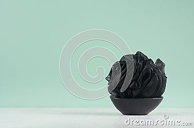 Style black accessorie for skin cleansing - bath sponge on black bowl on green mint menthe wall and white wood table. Stock Photo