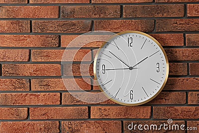 Stylish analog clock hanging on brick wall. Stock Photo