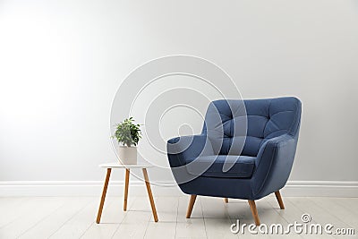 Stylish armchair and table with houseplant near wall. Interior design Stock Photo