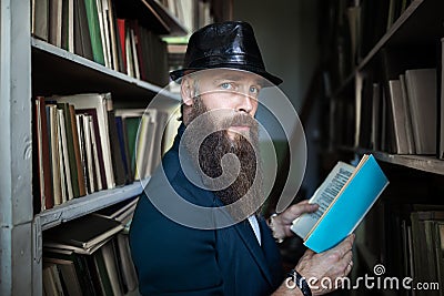 Stylish bearded man with book in library Stock Photo