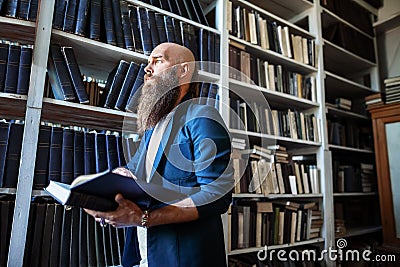 Stylish bearded man with book in library Stock Photo