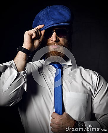 Bearded gentleman in white shirt and sunglesses holds his blue cap hat and tie greeting Stock Photo