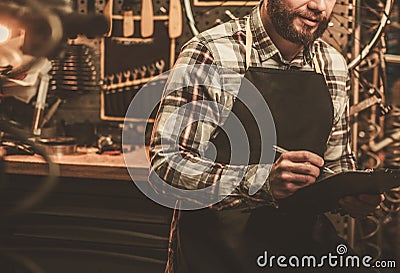 Stylish bicycle mechanic making notes in clipboard in his workshop. Stock Photo
