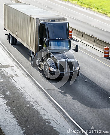 Stylish black big rig day cab semi truck with roof spoiler transporting cargo in container running on the straight divided highway Stock Photo