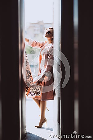 Stylish blonde girl in pink clothes and sunglasses posing in the city on a background of black huge barrels Stock Photo