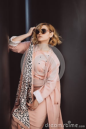 Stylish blonde girl in pink clothes and sunglasses posing in the city on a background of black huge barrels Stock Photo