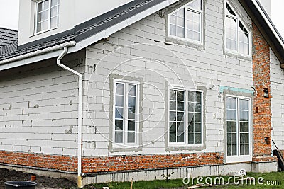 Stylish building with unfinished facade, white windows, modern black roof and dormer. Modern new farmhouse building exterior Stock Photo