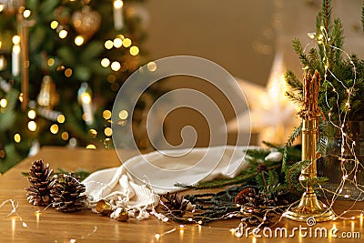 Stylish candle, golden lights, pine cones and ornaments on wooden table against stylish decorated christmas tree with festive Stock Photo