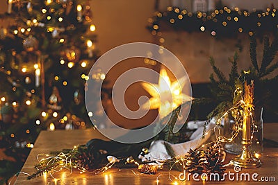 Stylish candle, golden lights, pine cones and ornaments on wooden table against stylish decorated christmas tree and fireplace Stock Photo