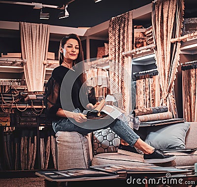 Modern designer is sittingon the sofa at her workplace surrounded by garments. Stock Photo