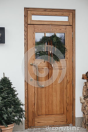 Stylish christmas rustic wreath with vintage bells and ribbon on wooden doors, fir tree and lantern on house exterior. Winter Stock Photo